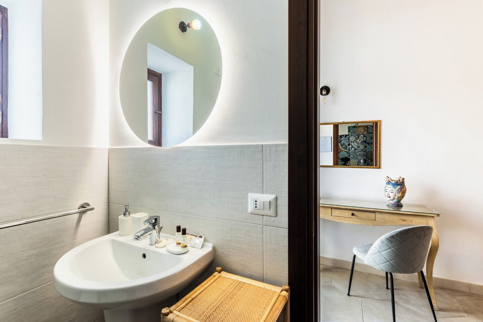 A modern bathroom with a large sink, a mirror, a toilet, and a vanity with a chair.