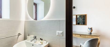 A modern bathroom with a large sink, a mirror, a toilet, and a vanity with a chair.