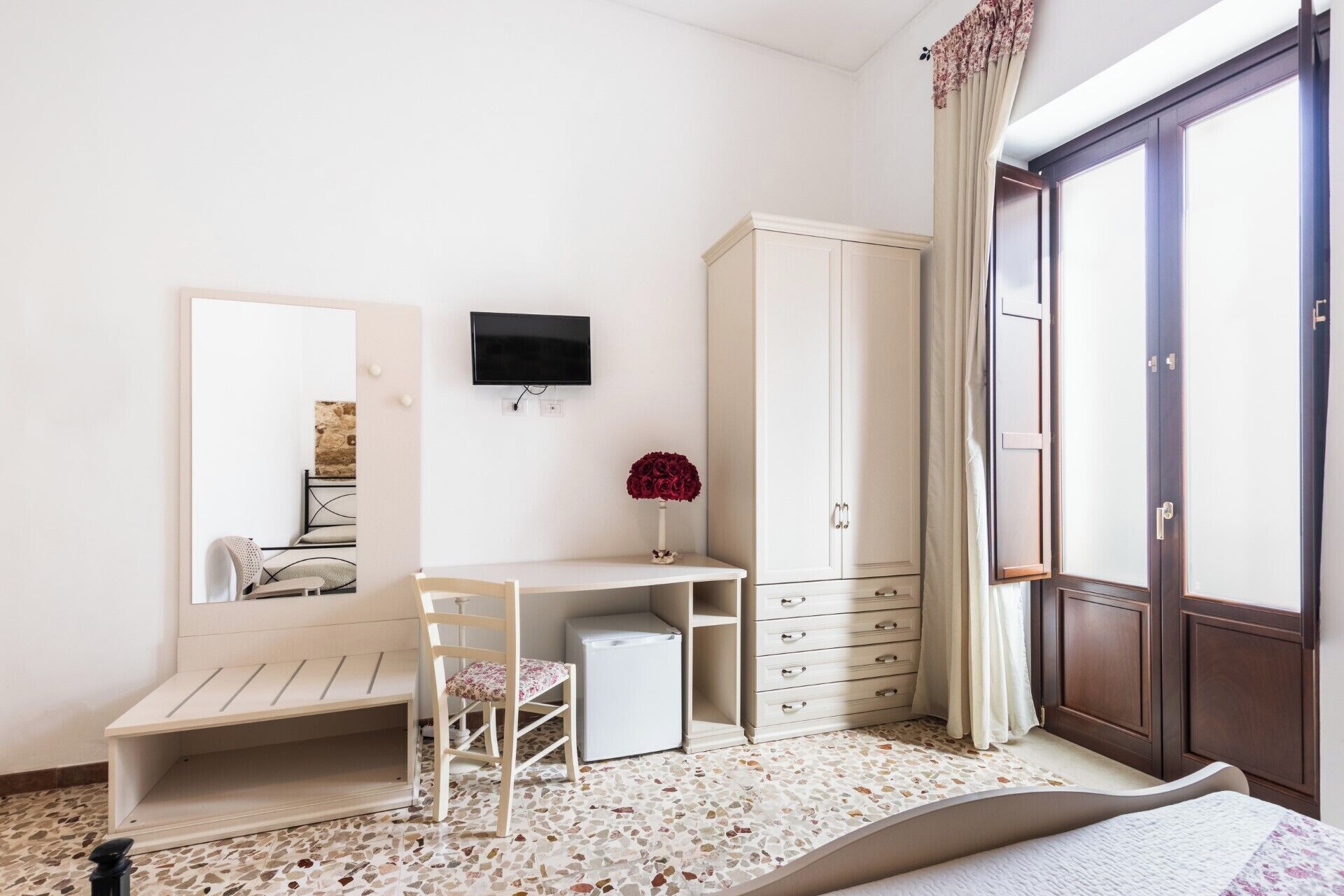 A bedroom with a bed, a desk, a chair, a wardrobe, a television, and a window with curtains.