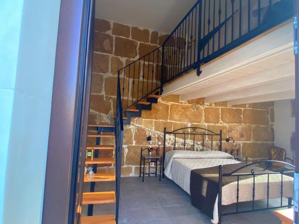 Une chambre avec un mur en pierre, un lit, une chaise et un escalier.