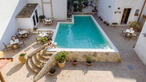 A rectangular pool with a stone border, surrounded by outdoor seating and potted plants. - Morfeo charming Rooms & relax (Avola)