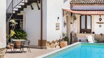 A poolside area with a staircase leading to a second floor, a small outdoor table with chairs, and a decorative wall with a sign.