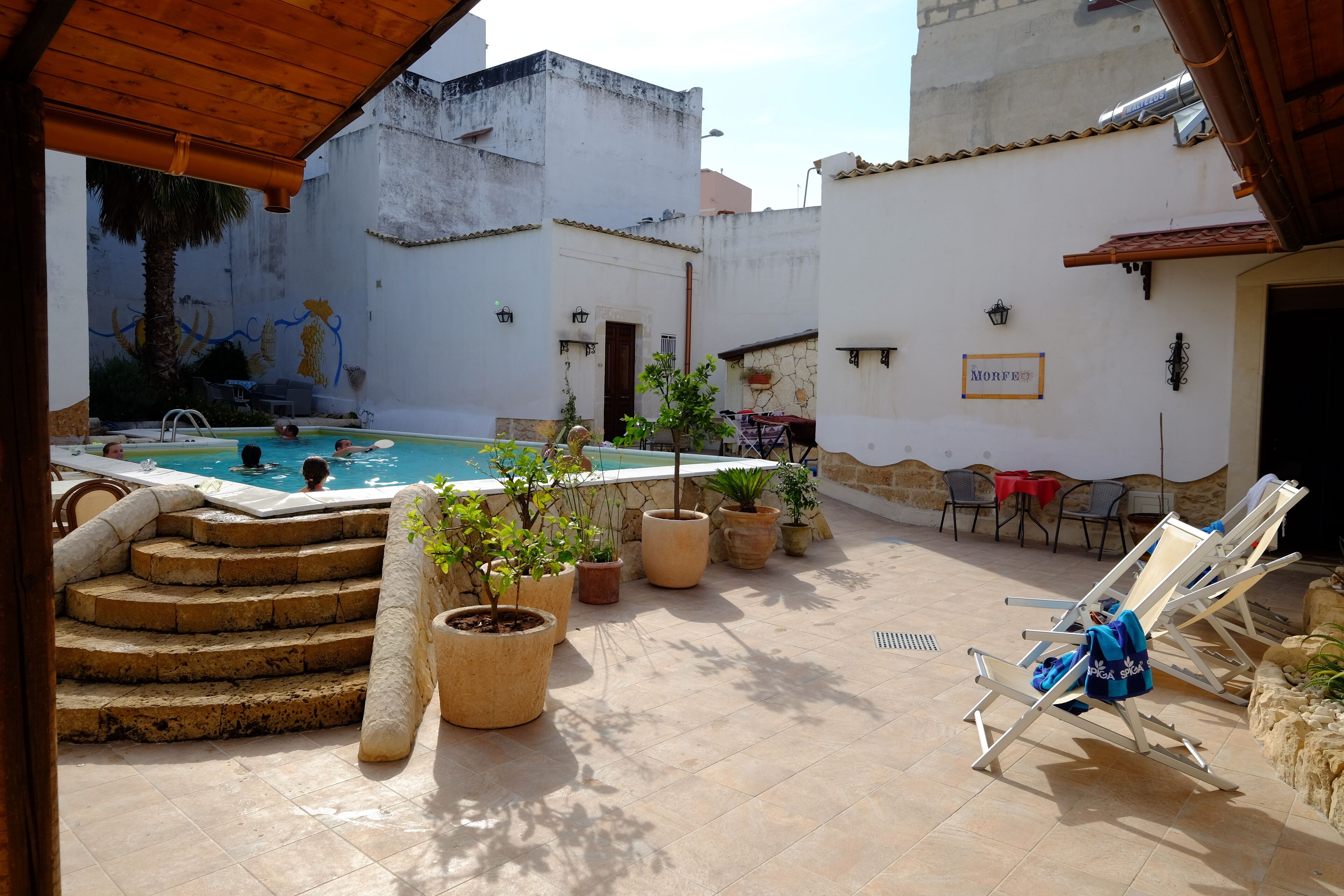 Un espace piscine avec des marches descendant vers l’eau, entouré de plantes en pot et de chaises longues.