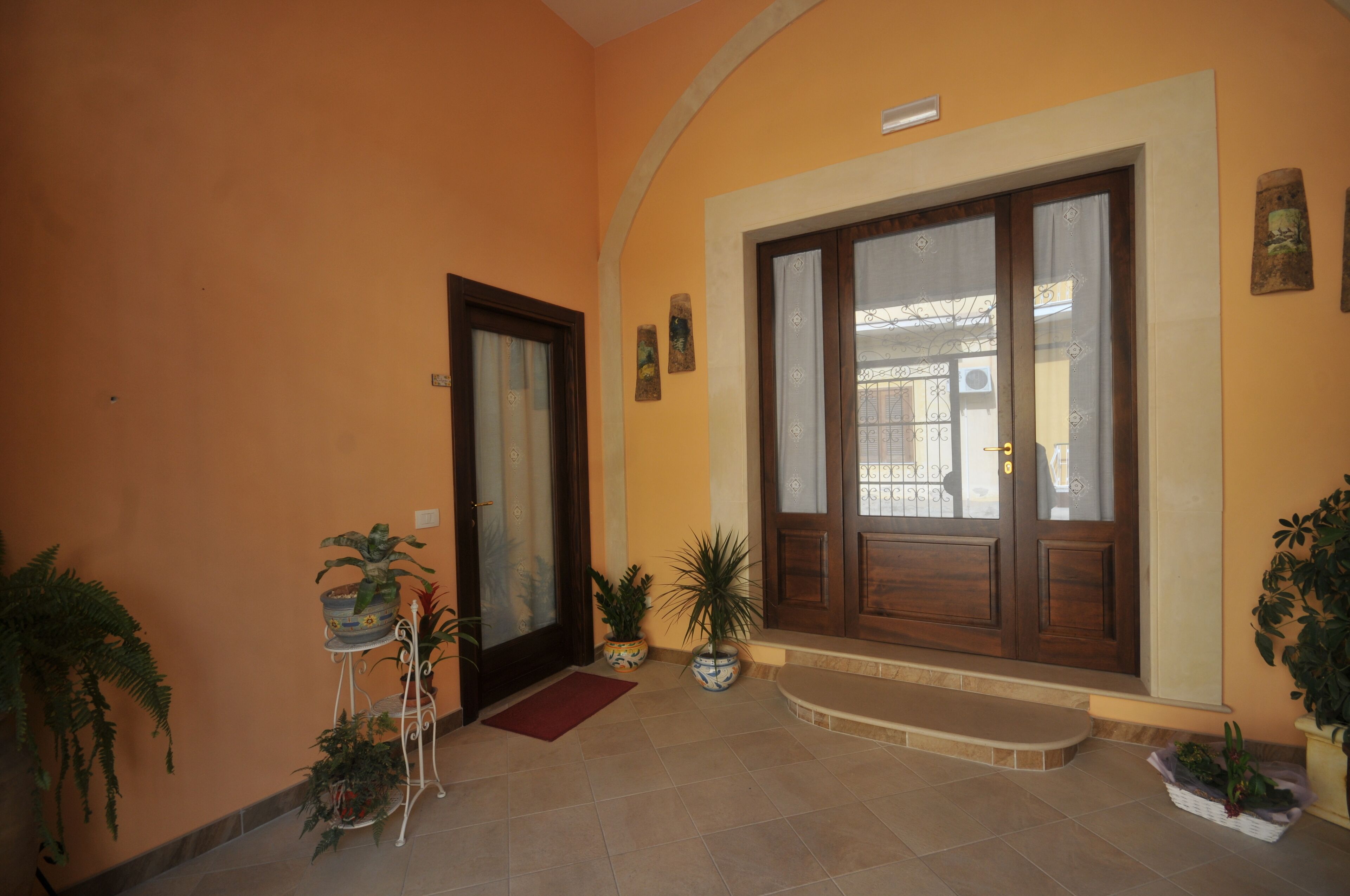 A hallway with a wooden door, potted plants, and a tiled floor.
