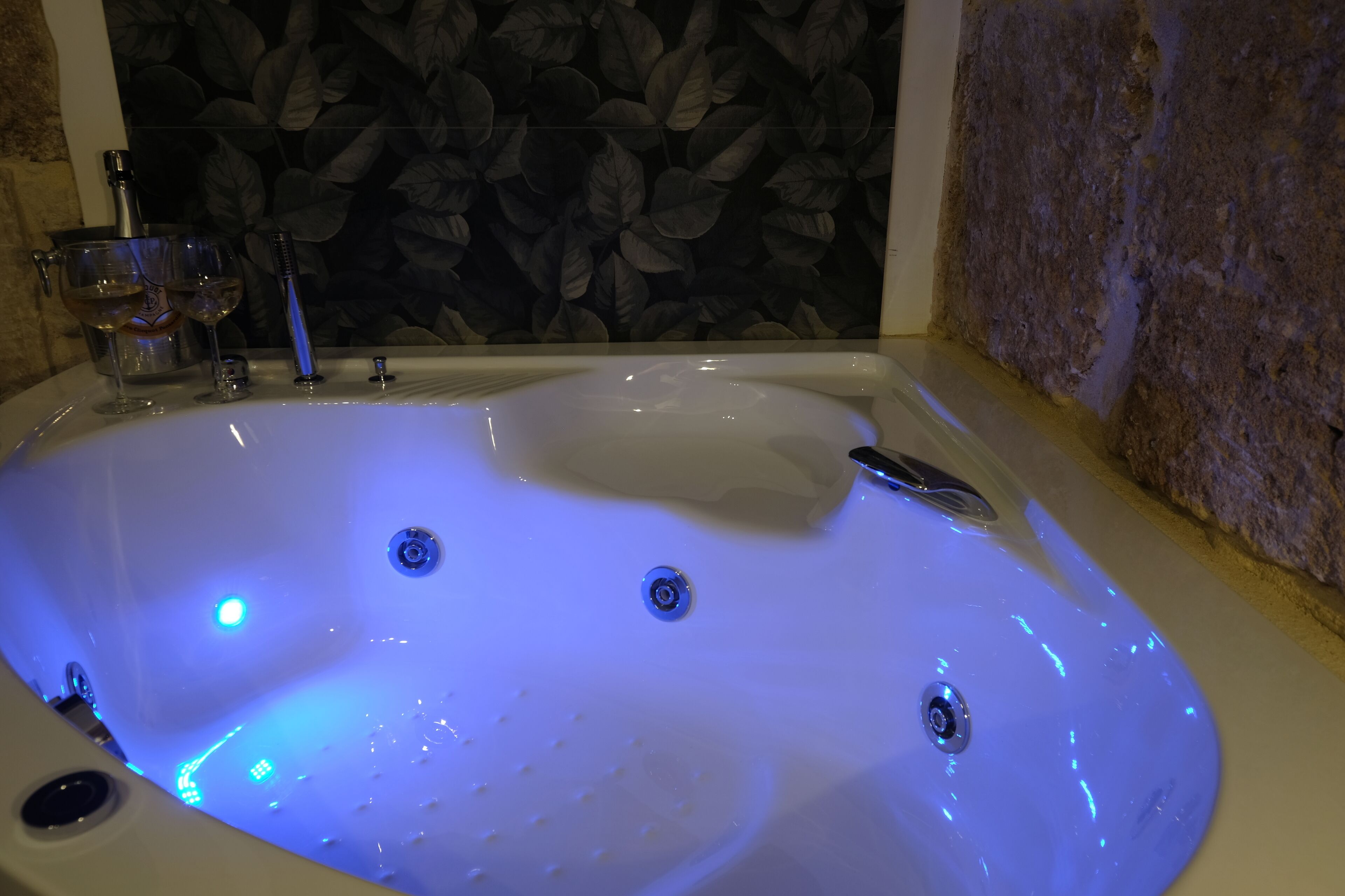 A bathtub with blue lighting, a wine glass, and a bottle.