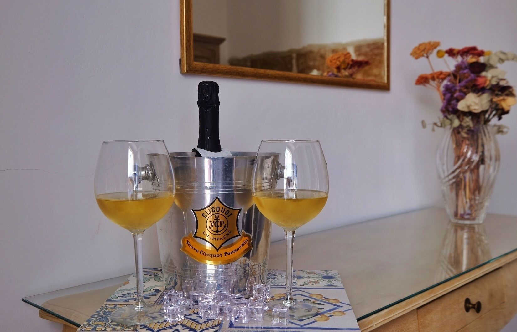 A bottle of Veuve Clicquot champagne, two glasses, and a vase with flowers on a table.
