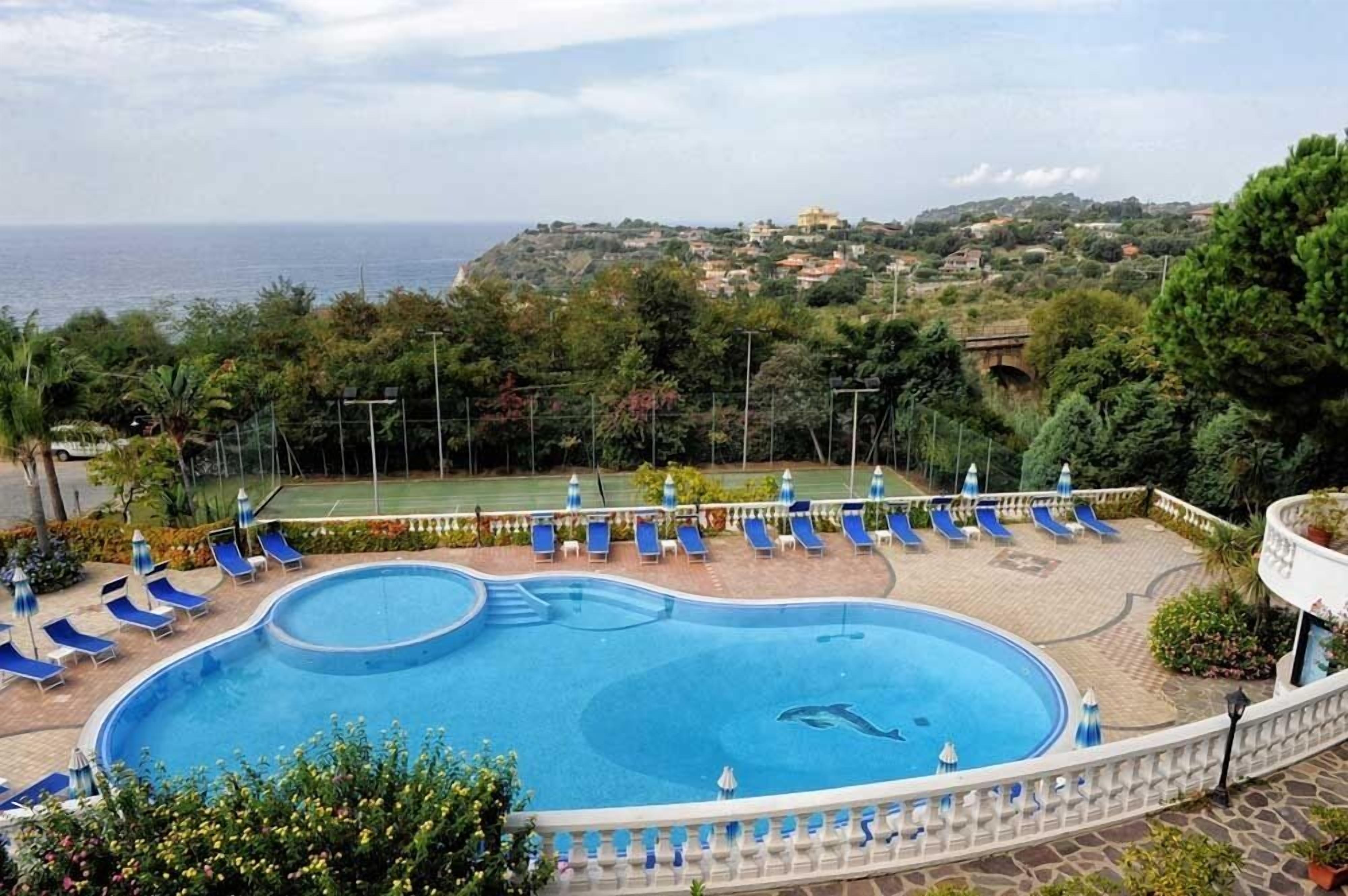 Una piscina con sillas reclinables azules y vista al mar y colinas al fondo.