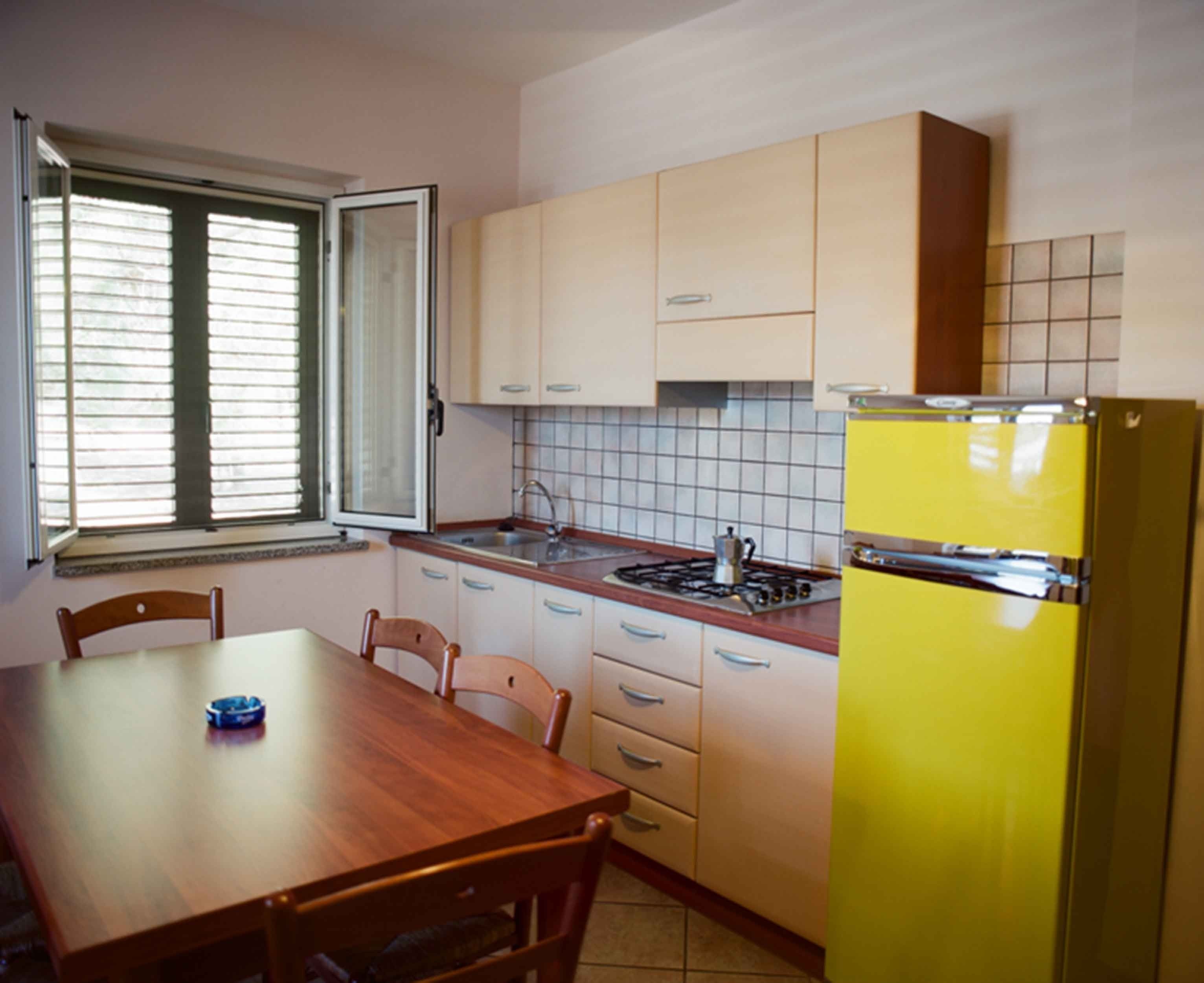 Eine Küche mit Holztisch, Stühlen, einem gelben Kühlschrank und hellen Schränken.