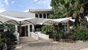 A stone-paved courtyard with outdoor seating and umbrellas, leading to a building with arches and a staircase.