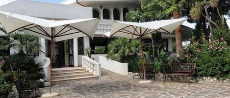 A stone-paved courtyard with outdoor seating and umbrellas, leading to a building with arches and a staircase.