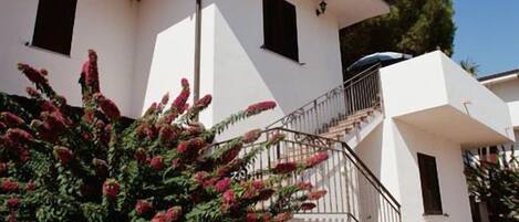 A modern two-story house with a white exterior, a staircase with a metal railing, and a small balcony.
