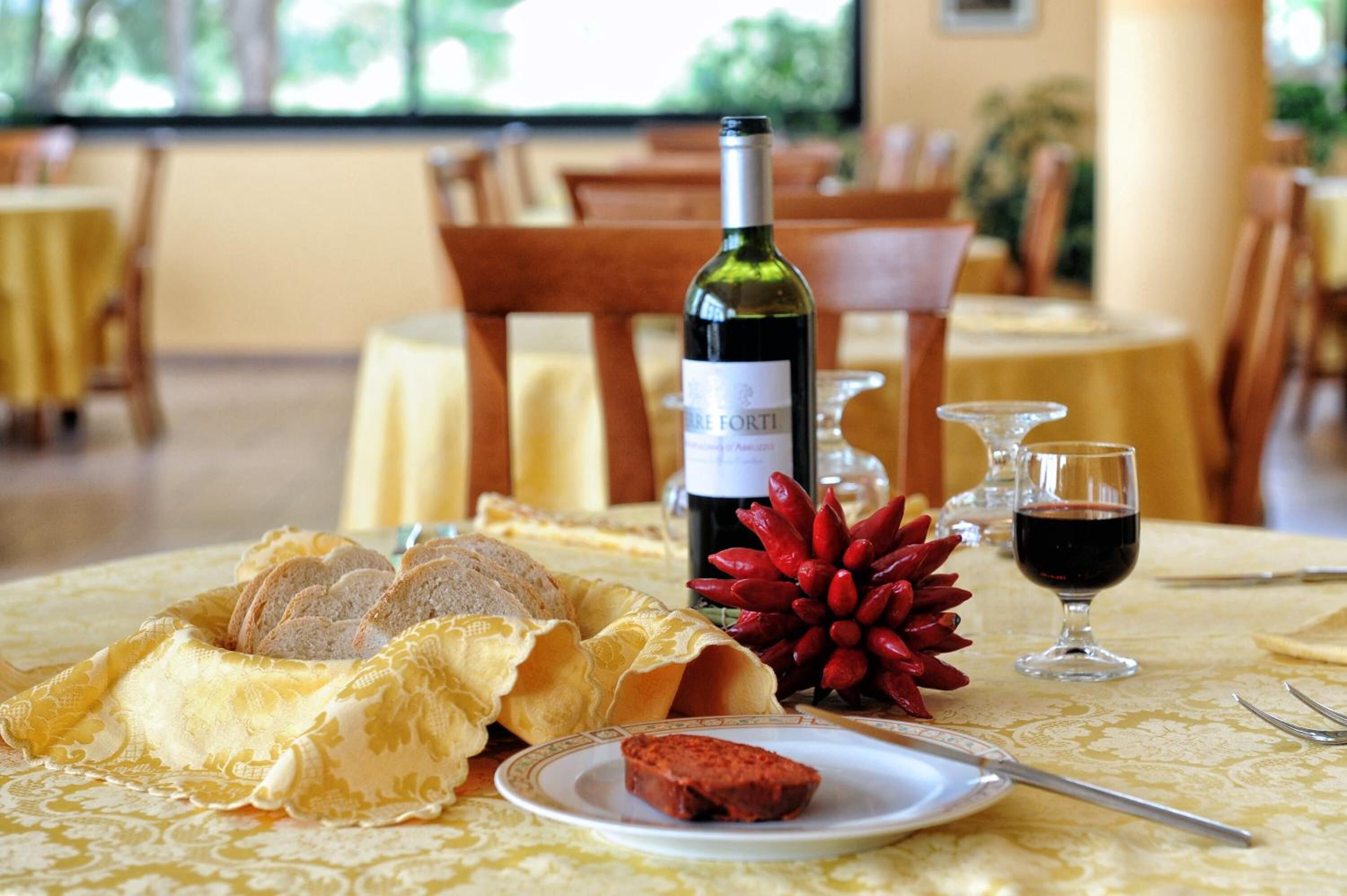 Una mesa de comedor con pan, una botella de vino y una copa de vino tinto.