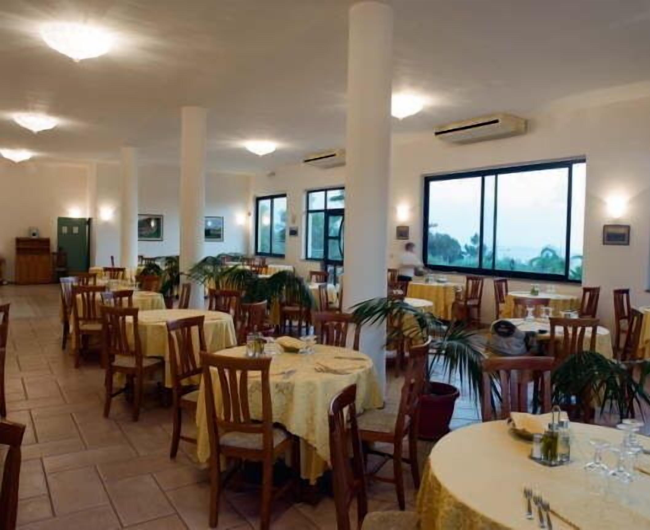 A spacious dining area with multiple tables and chairs, large windows offering a view, and an air conditioning unit on the wall.