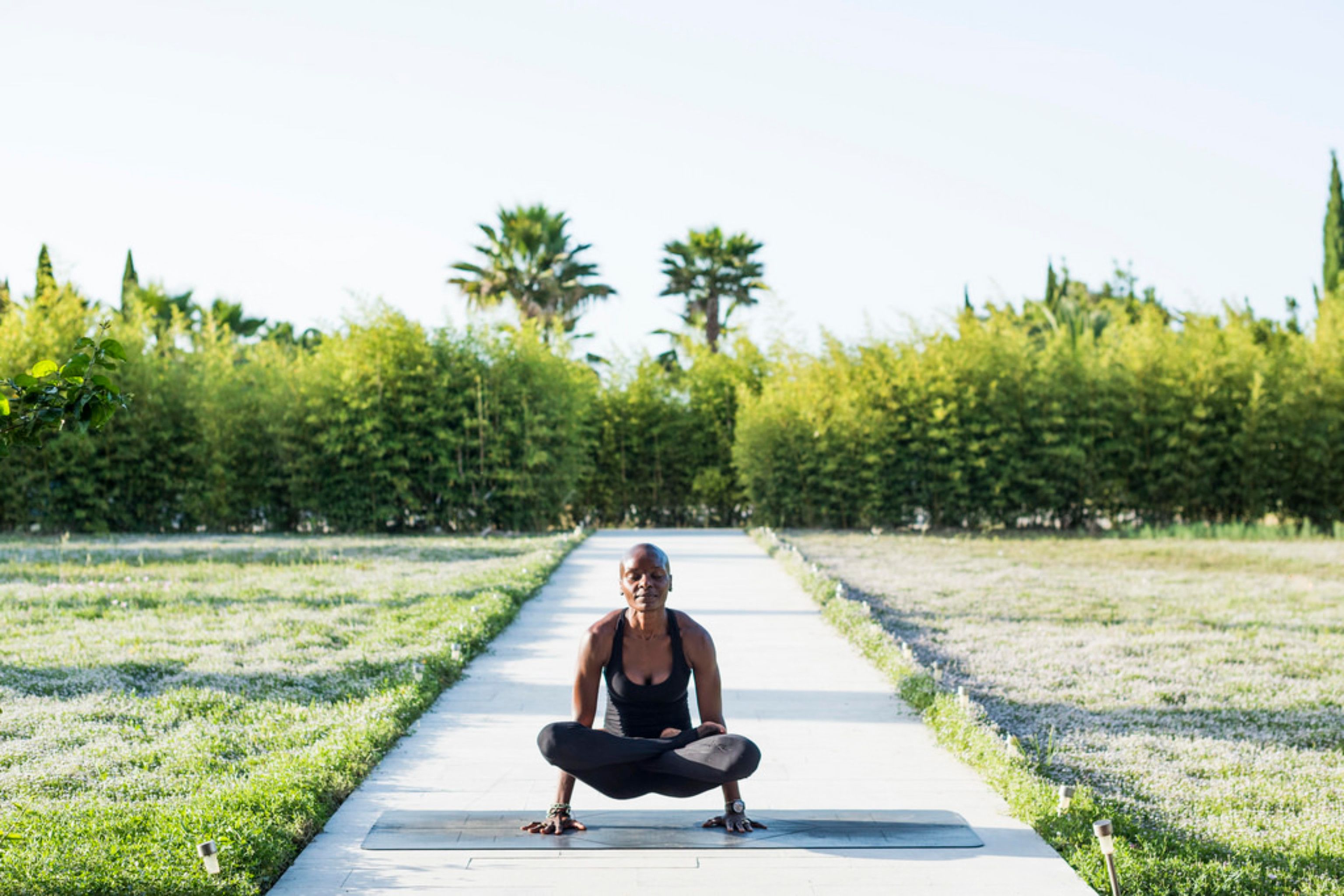 Una persona realizando una postura de yoga en un sendero rodeado de vegetación.