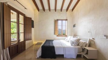 Ein Schlafzimmer mit Bett, Nachttisch, Lampe, Fenster und Holzbalken an der Decke.