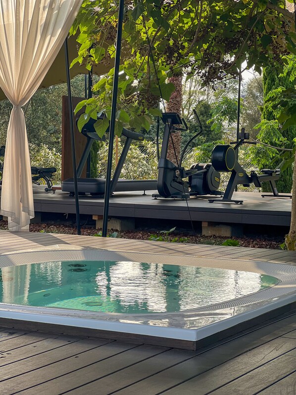 Una piscina con equipo de ejercicios, una zona cubierta y un árbol.