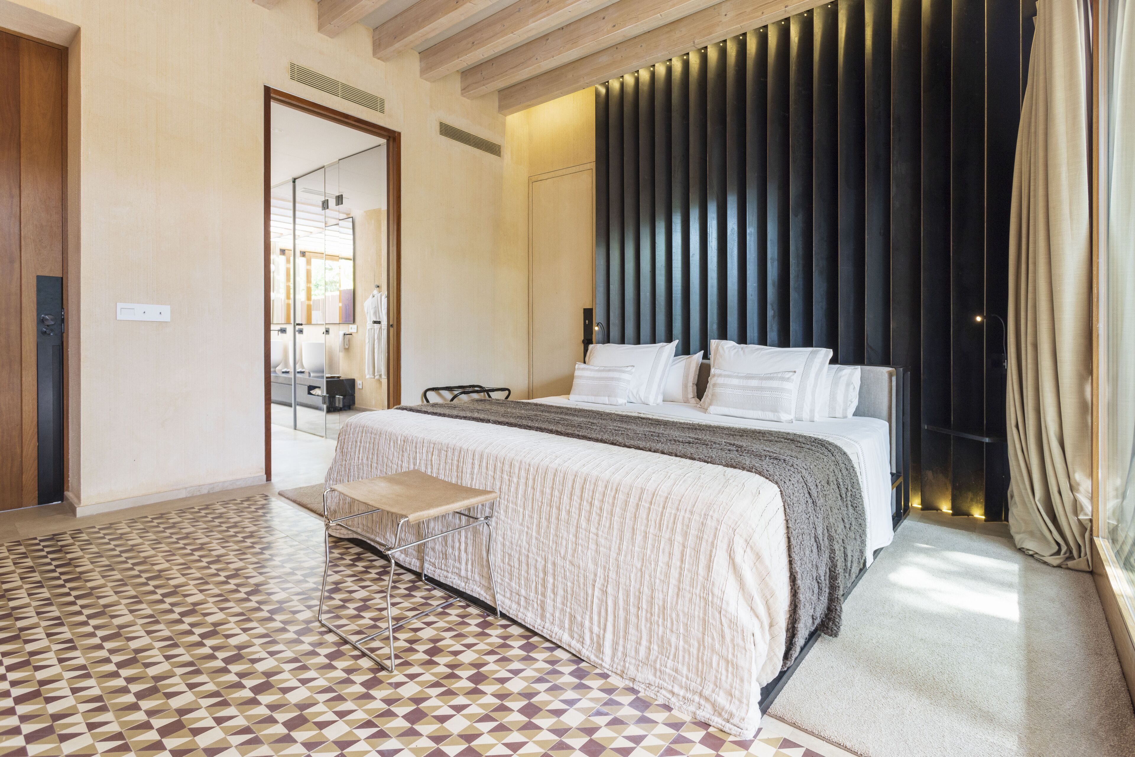 A modern hotel room with a large bed, a small table, and a patterned floor.