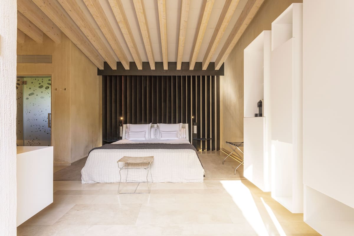 A modern bedroom with a large bed, a bench, and a minimalist design.