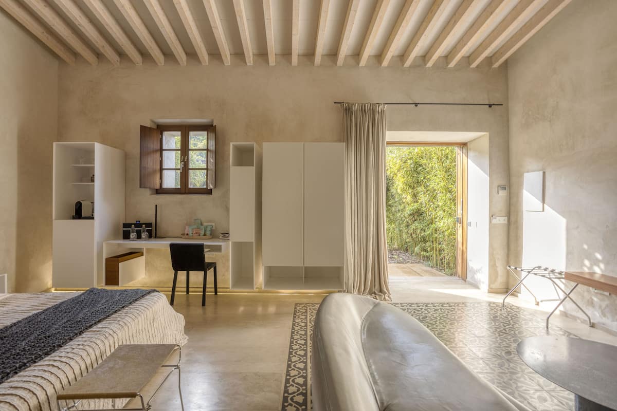 A modern bedroom with a bed, a desk, and a view of greenery outside.