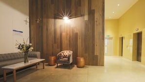 Zona de recepció amb paret de fusta, un sofà, una cadira, una taula i dues làmpades de peu.