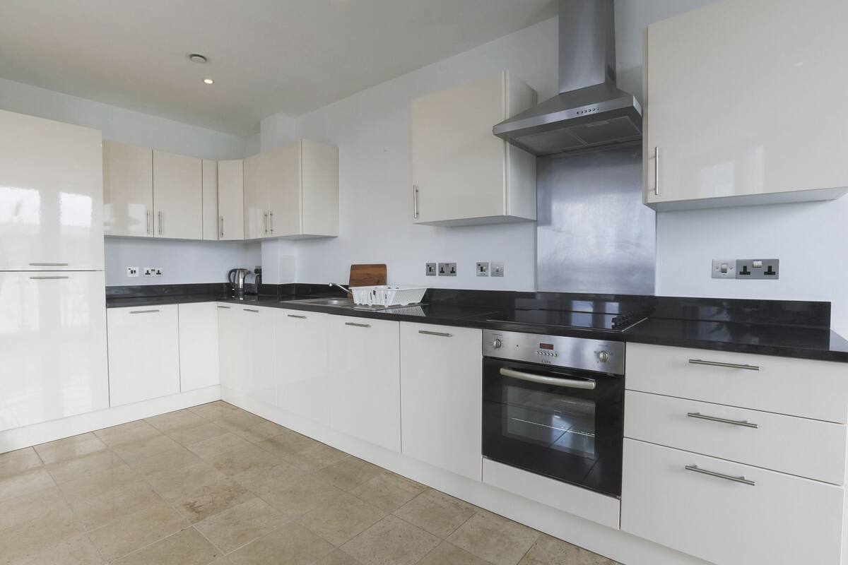 A modern kitchen with white cabinetry, a black countertop, and stainless steel appliances.