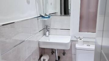 A compact bathroom with a white sink, two hair dryers mounted on the wall, a toilet, and a trash bin.