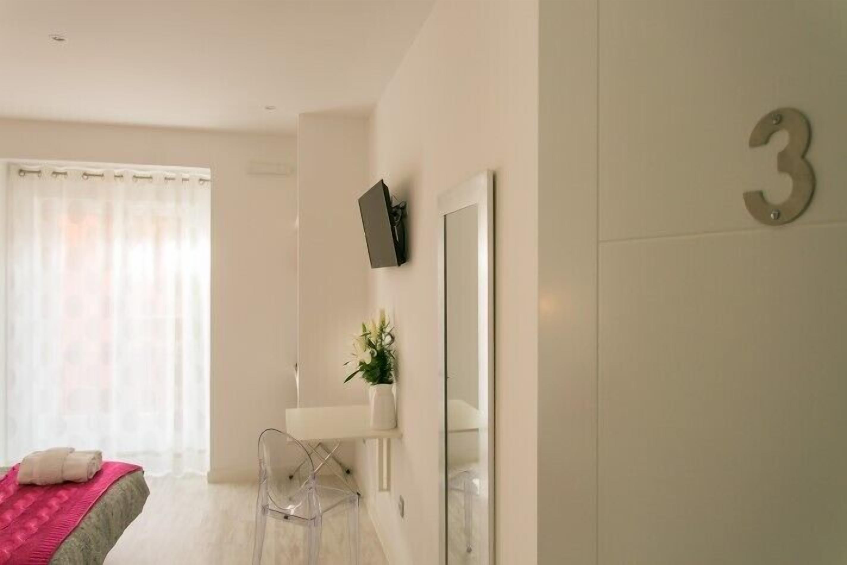 A modern hotel room with a bed, a small desk, a mirror, and a number '3' on the wall.