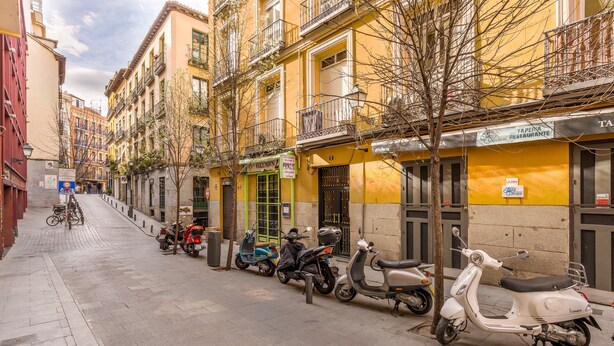 A narrow street lined with yellow buildings, parked scooters, and a few bicycles. - Hostal Met Madrid (Madrid)