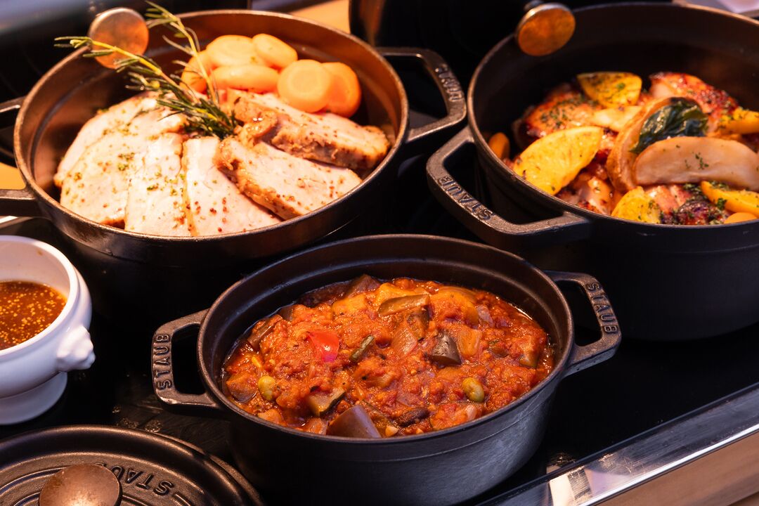 A stove with three pots containing various dishes, including a stew and sliced meat with vegetables.