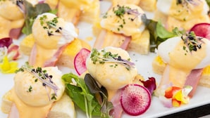 A dish with poached eggs, ham, and greens, garnished with herbs. - Orient Hotel Kochi (Kochi)