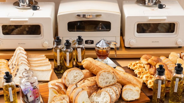 A kitchen with two BalmuDA ovens, a wooden cutting board with sliced bread, and bottles of oil. - Orient Hotel Kochi (Kochi)