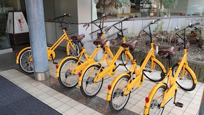 A row of yellow bicycles parked in an indoor area with tiled flooring and a metal pillar. - Orient Hotel Kochi (Kochi)