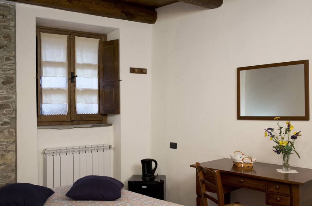 Un dormitorio con cama, un escritorio de madera, un espejo, un radiador y una ventana con cortinas.