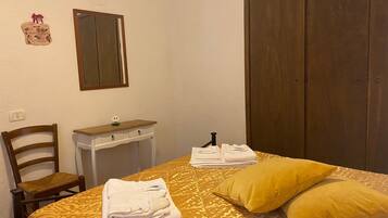 Una habitación de hotel con cama, una silla de madera, una mesita de noche con espejo y un armario.