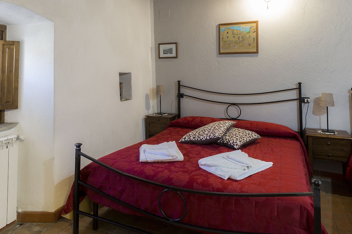 Ein Schlafzimmer mit Holzbalkendecke, einem Metallbettgestell, einer roten Bettdecke und einem Nachttisch mit Lampe.