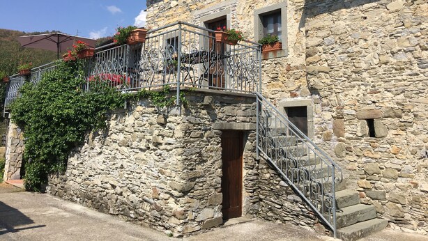 Un edificio de piedra con balcón, escaleras y plantas en macetas.