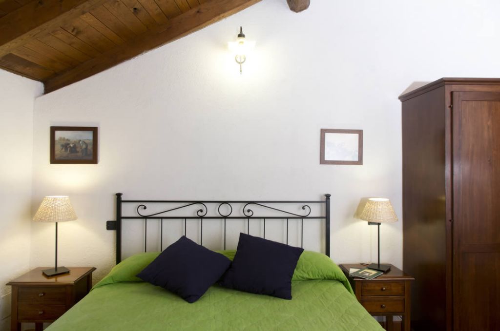 Un dormitorio con una cama, dos mesitas de noche, un armario de madera e iluminación en el techo.
