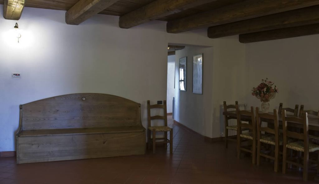 A room with a wooden bench, a dining table with chairs, and a vase with flowers.