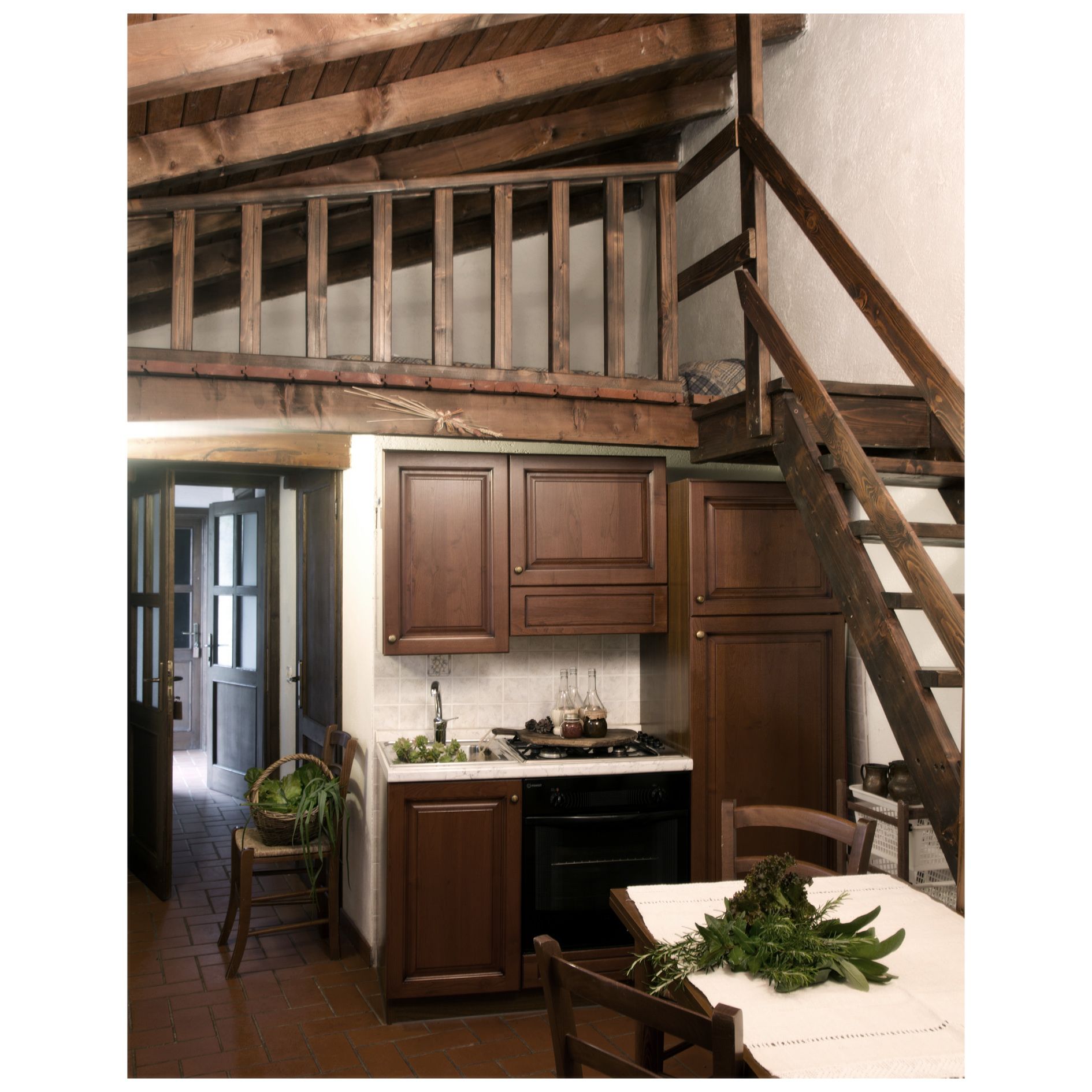 Eine rustikale Küche mit Holzbalken, einem Esstisch mit weißer Tischdecke und einer Treppe.
