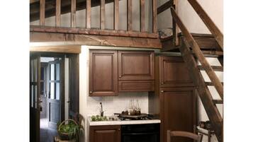Eine rustikale Küche mit Holzbalken, einem Esstisch mit weißer Tischdecke und einer Treppe.