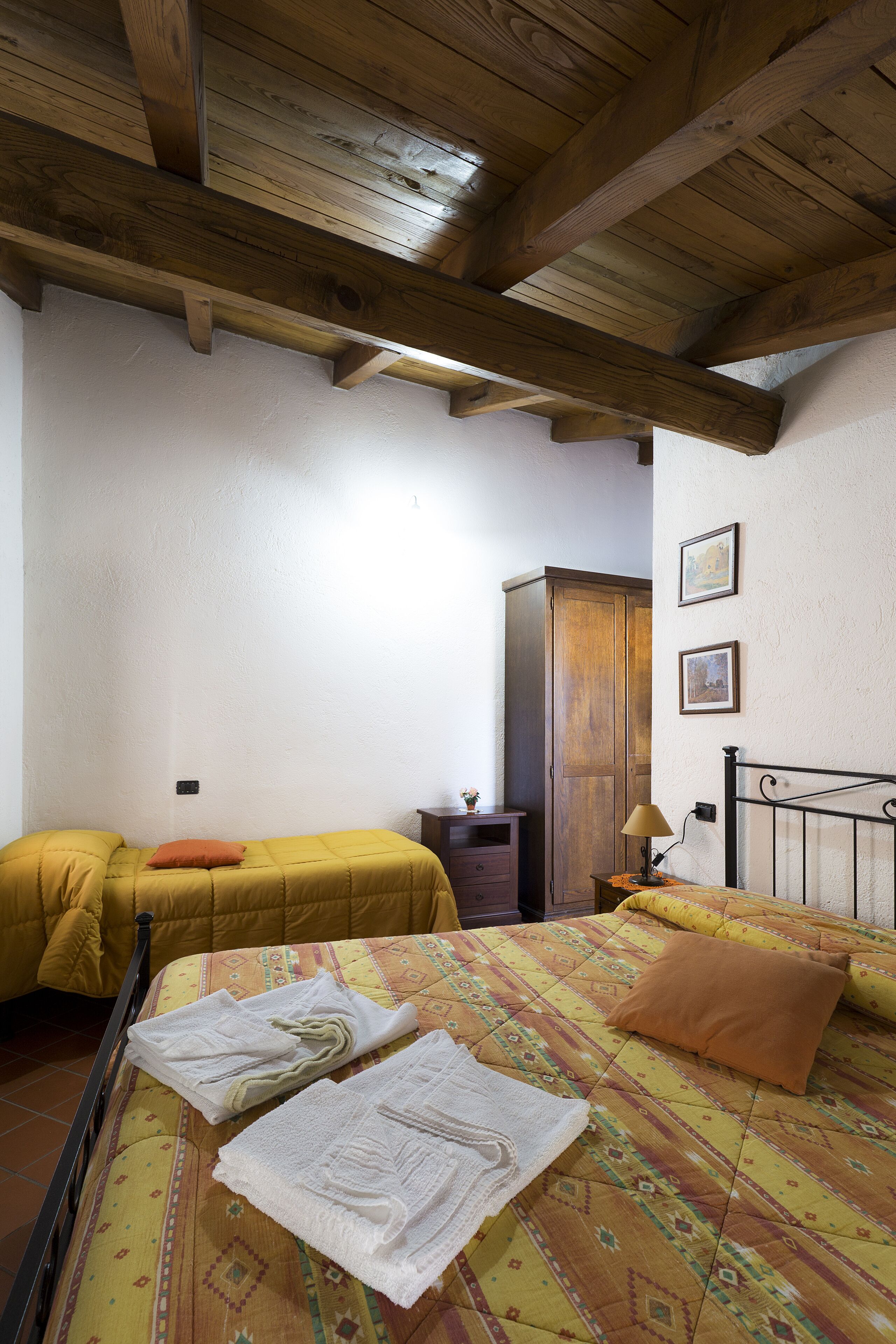 Een kamer met een bed, een houten garderobe en een klein tafeltje met een lamp.