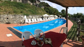 Zona junto a la piscina con pared de piedra, sillones blancos para tomar el sol y una mesa con comida y bebidas.
