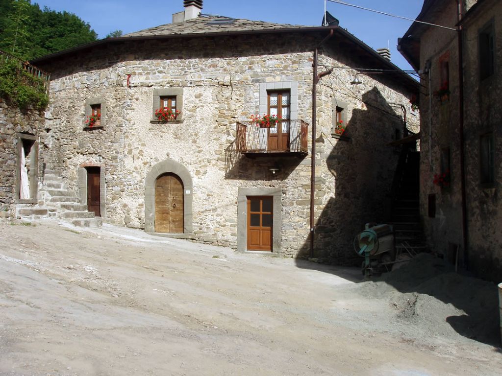 A stone building with a wooden door, a small balcony with flowers, and a staircase leading to the entrance.