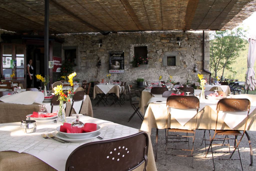 An outdoor dining area with stone walls, tables set with white tablecloths, and chairs.