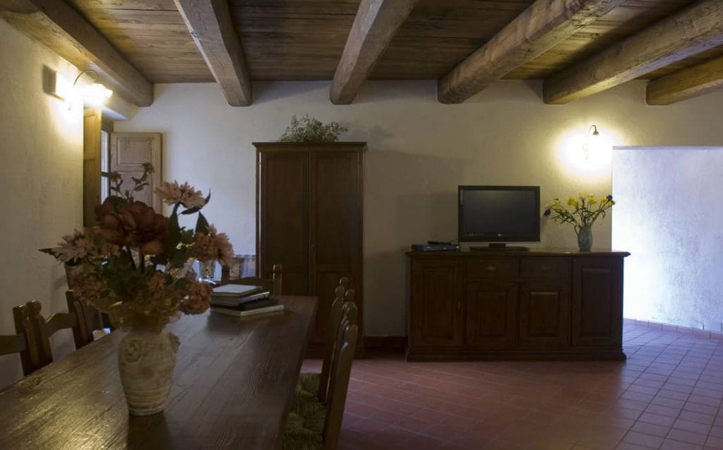 Een eetgedeelte met een houten tafel, stoelen, een bloemenvaas, een kast en een televisie.