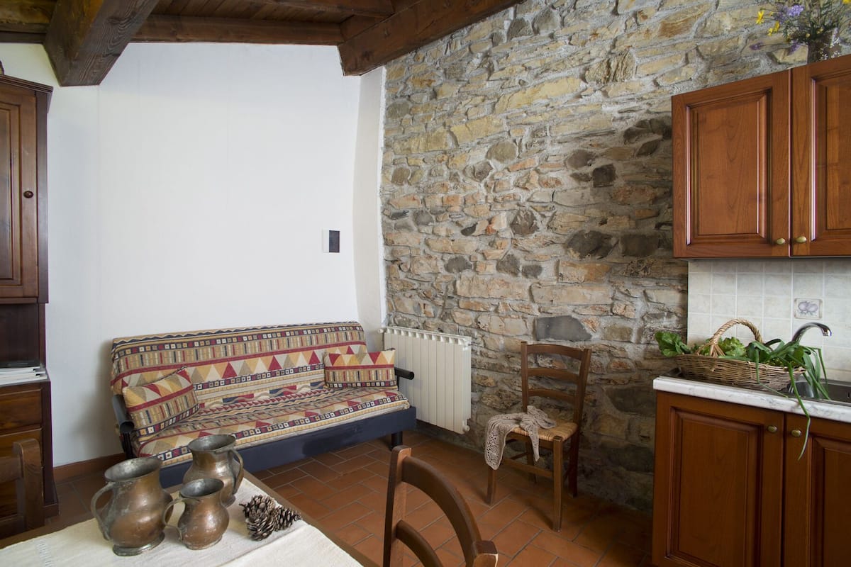 Eine gemütliche Küche mit Steinwand, Holzschränken, einem gemusterten Sofa und rustikalen Einrichtungsgegenständen.