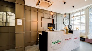 Een receptiebalie met 'Belvilla by OVO' branding, een modern ontwerp met een marmeren afwerking en een groot raam dat natuurlijk licht binnenlaat.