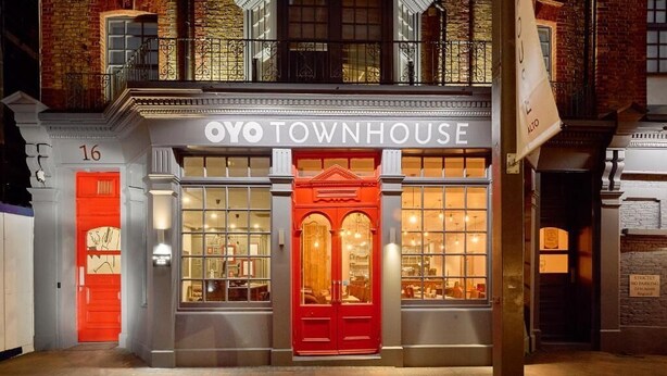 Een gebouw met een bord waarop 'OYO TOWNHOUSE' staat en een rode deur.