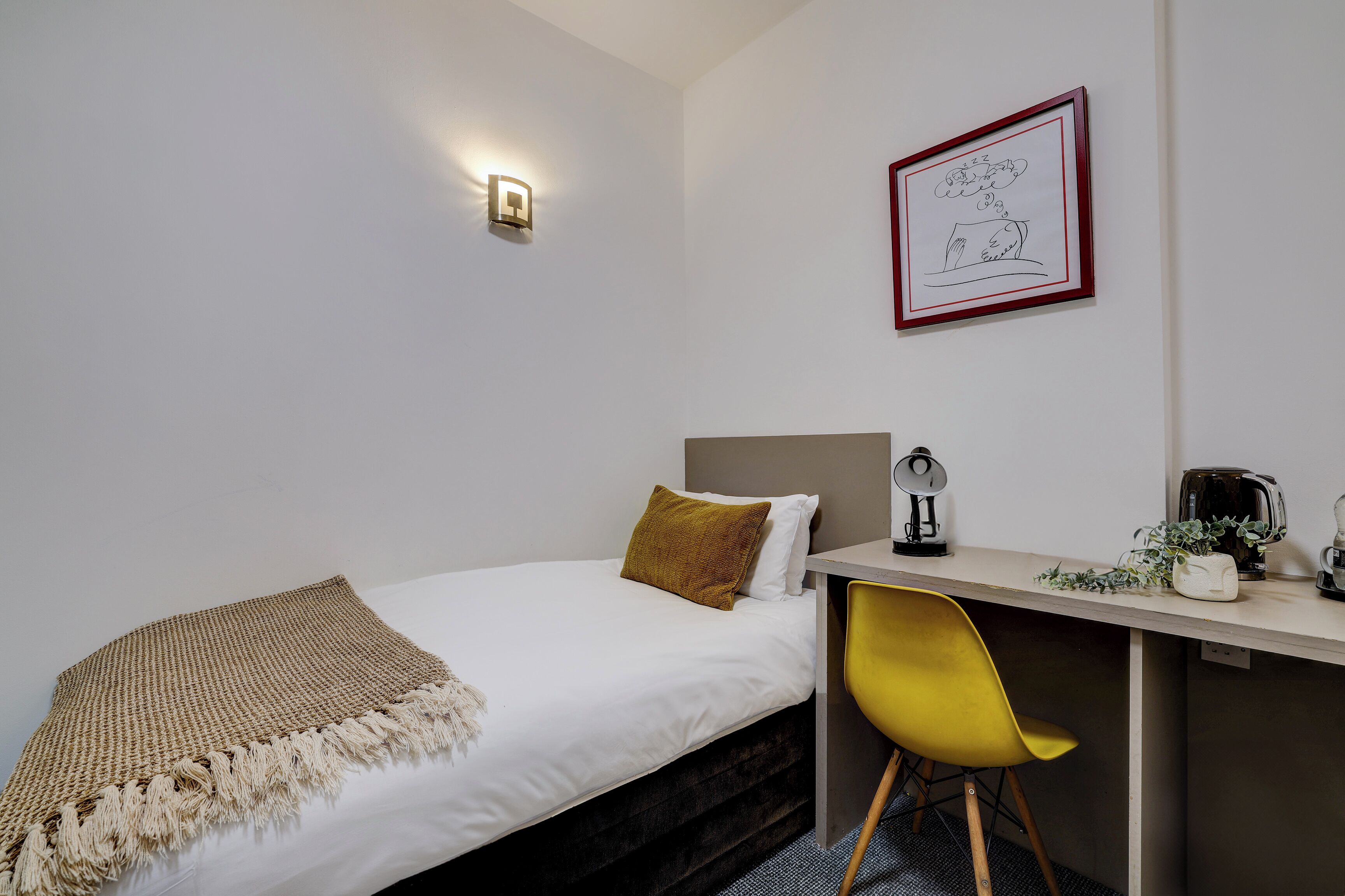 Une chambre à coucher avec un lit, un bureau, une chaise, une lampe et un tableau encadré au mur.