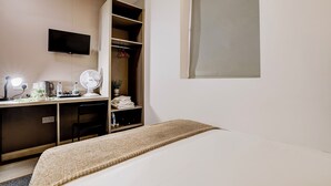 Een slaapkamer met een bed, een bureau met een computer, een stoel, een kledingkast en een aan de muur bevestigde televisie.